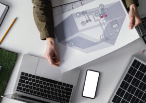 طراحی نقشه برق صنعتی در کنار لپ‌تاپ، موبایل و تجهیزات انرژی خورشیدی روی میز کار مهندس